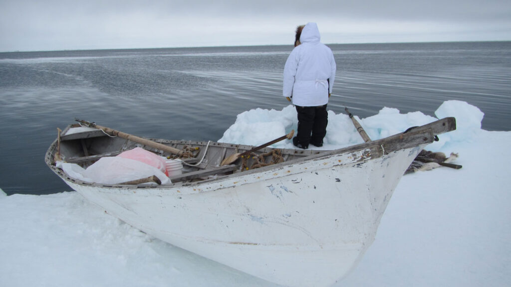 A person faces the sea from an ice floe where a kayak is docked.