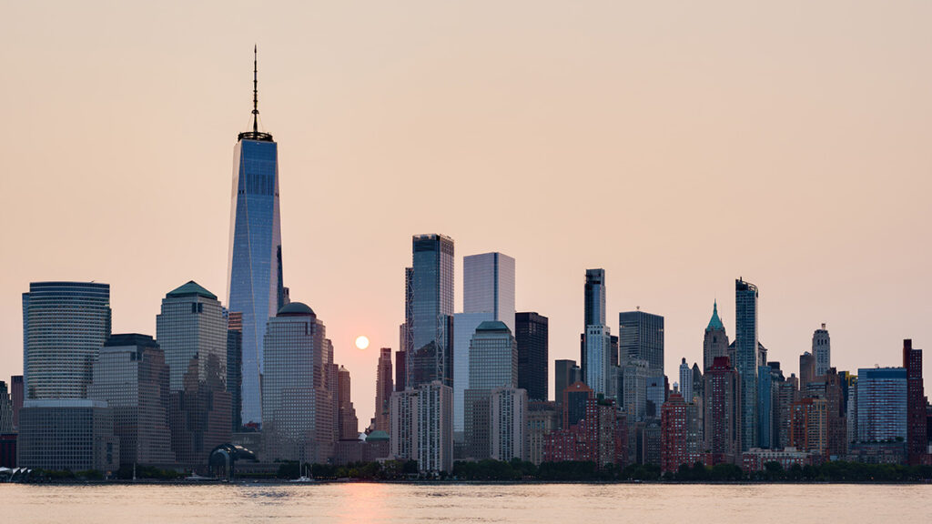 The sun rises in a pink sky beyond the skyline of lower Manhattan.