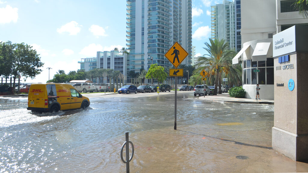 A van drives through a flooded street in downtown Miami on a sunny day.