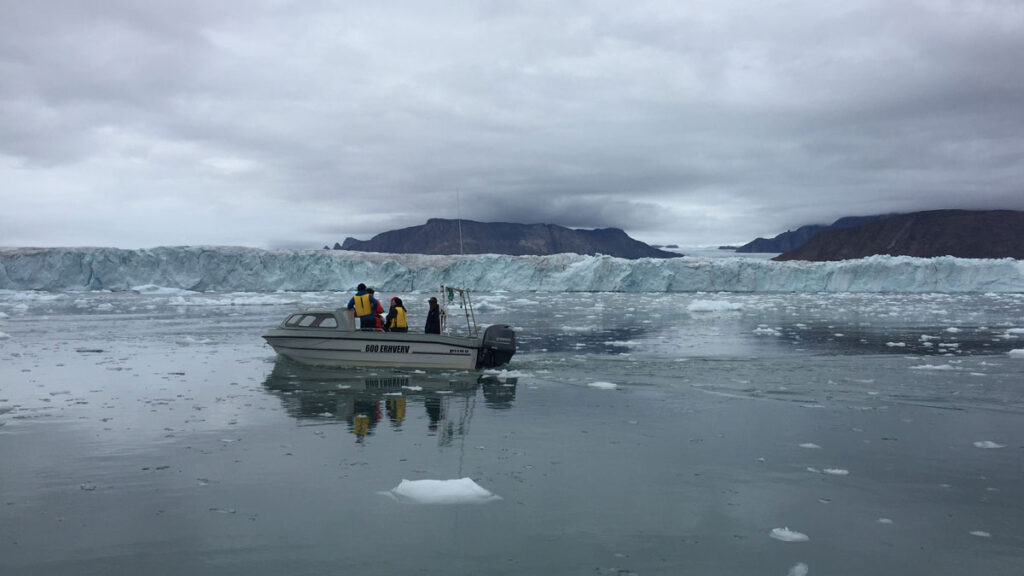 Several people aboard a small motorboat in a fjord with a glacial ice cliff in the background