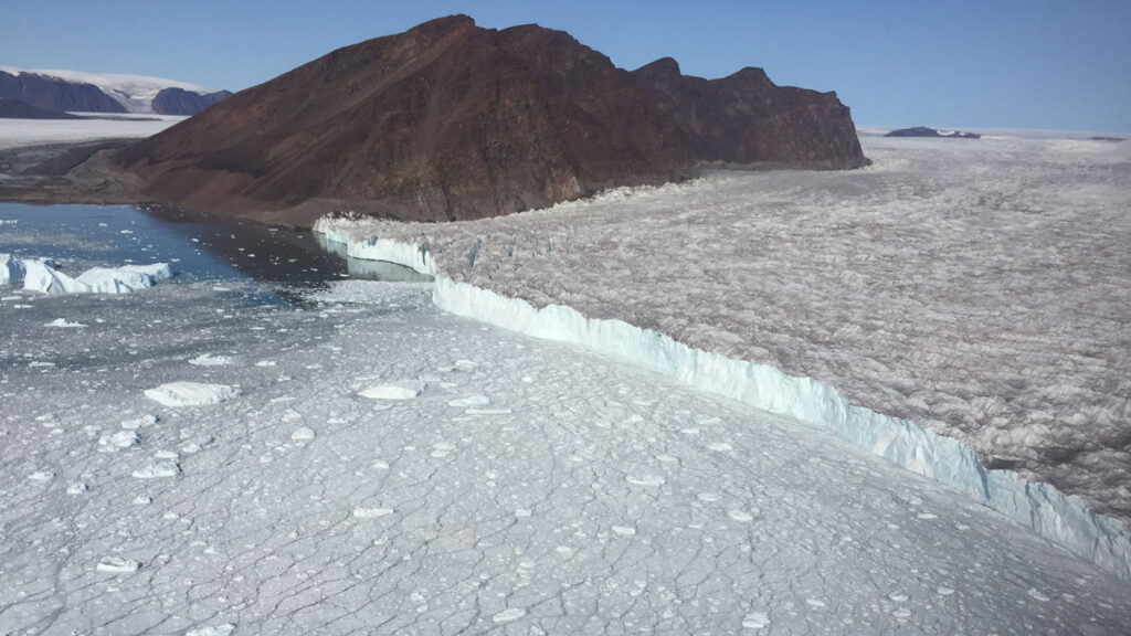 Aerial view of a glacial terminus with sea ice and icebergs floating in the water near the glacier