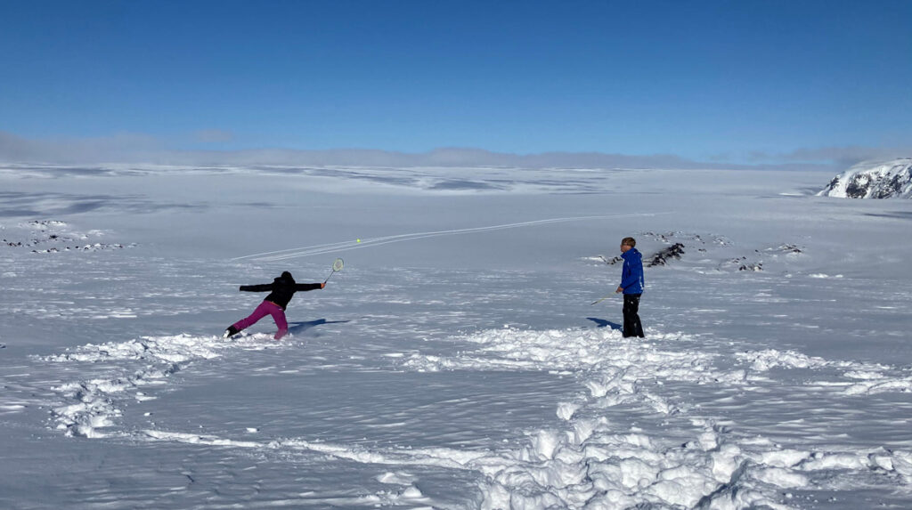 Two people play badminton on a vast snow-covered expanse.