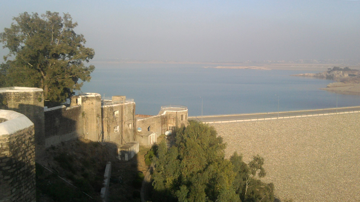 A dam impounds a large reservoir (background) as seen from a stone fort (foreground).