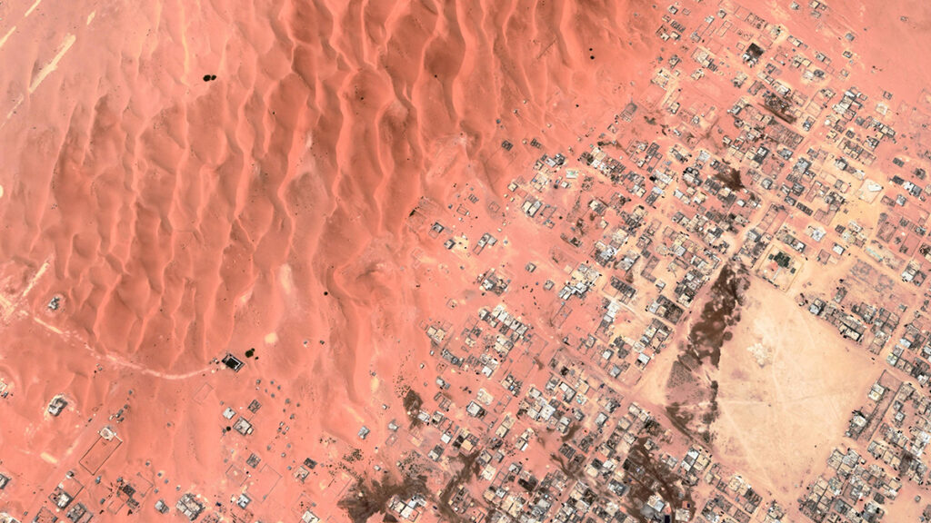 An aerial image of orange sand dunes overtaking buildings.