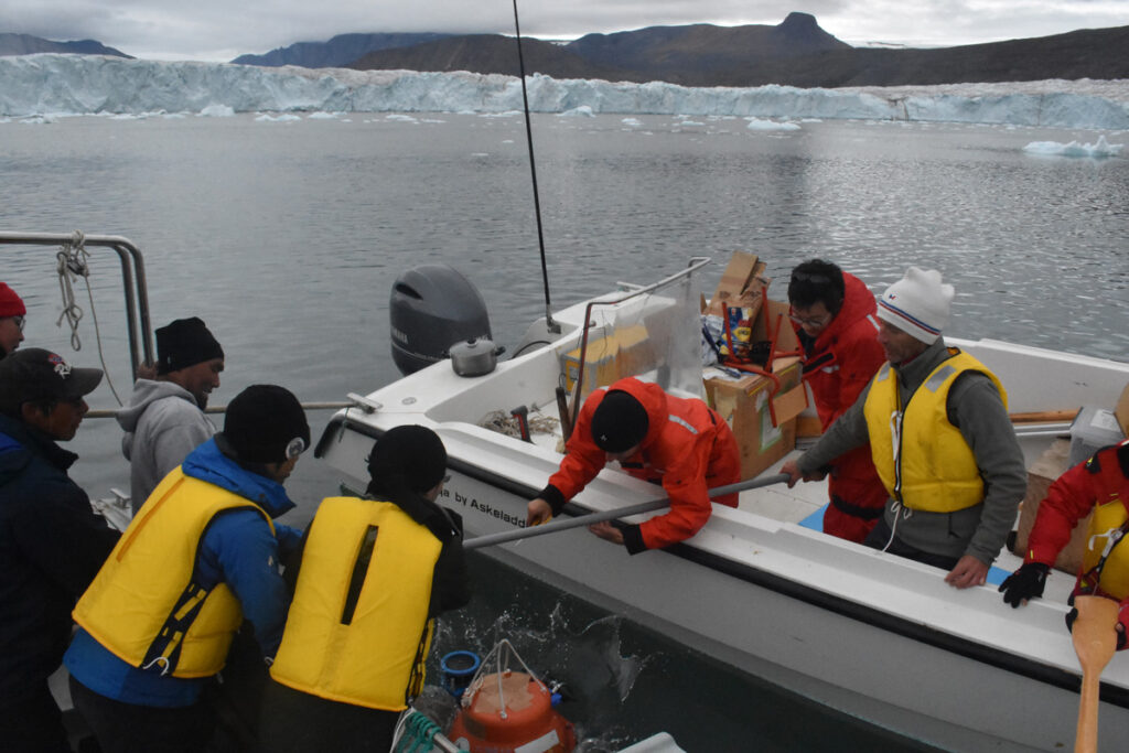 People hold a rod between two motorboats in a glacial fjord to drop a scientific instrument into the water