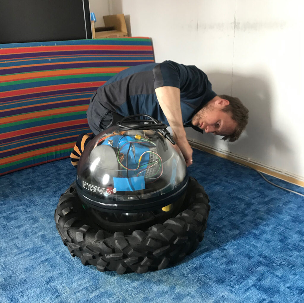 A researcher crouches by an ocean bottom seismometer on a carpeted floor