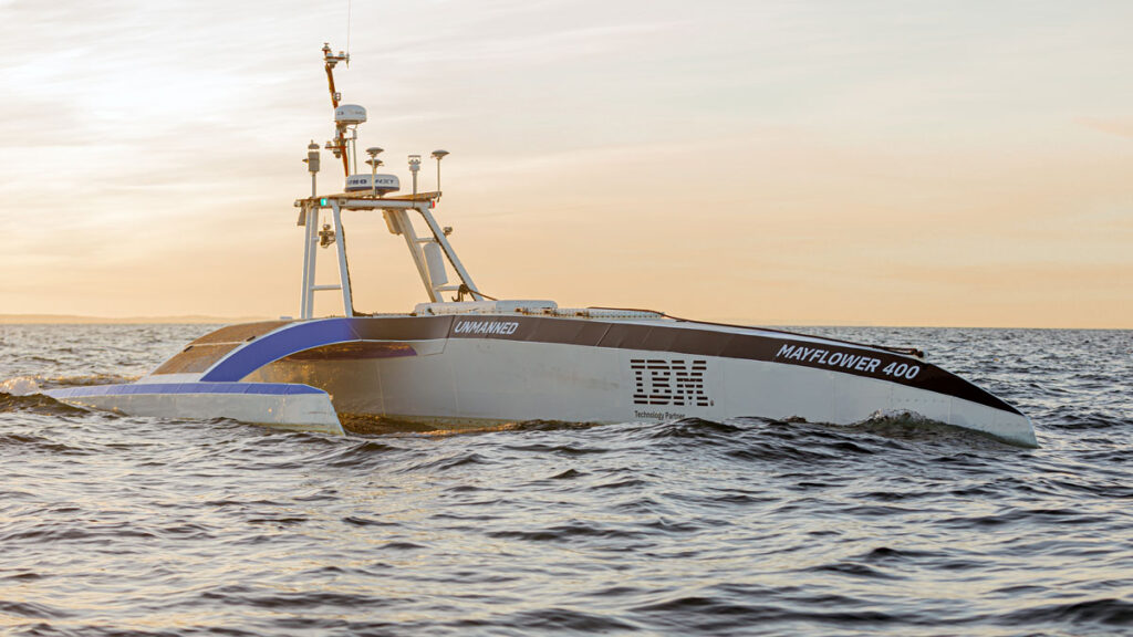 A white craft with blue trim floats on the ocean before a peach-colored sky