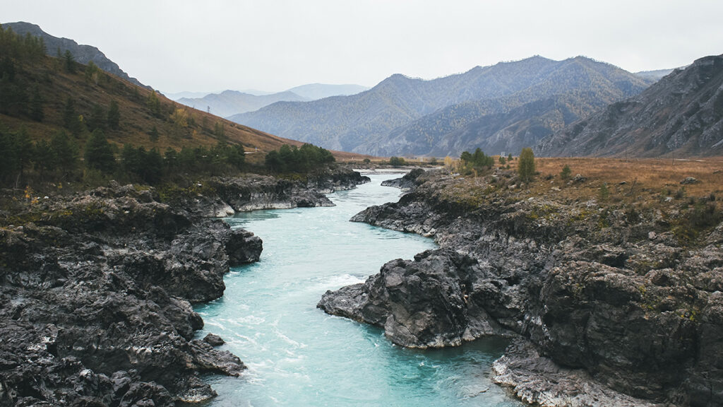 A river in southern Siberia flows between rocky banks toward mountains in the distance.