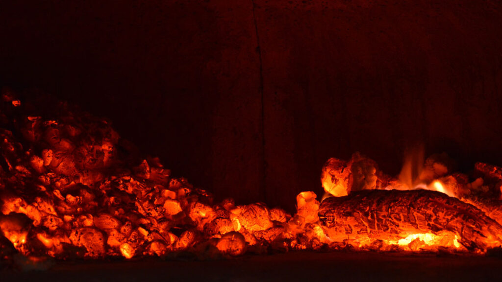 Coals smolder in a dark fireplace.