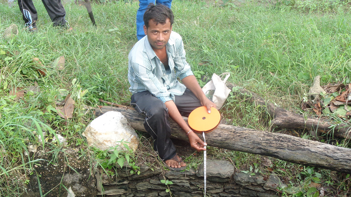A man measuring the water level in an open well with a measuring tape