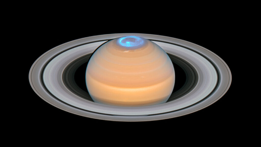 A blue ring of auroral emission glows above Saturn’s north pole.