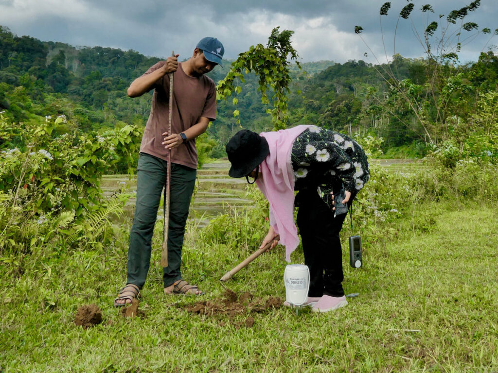 Two students dig a hole to deploy a seismic instrument in a green farm field