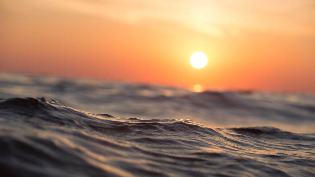 Close-up of ocean waves with the Sun setting in the background.