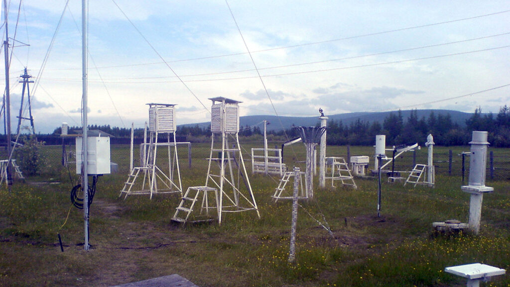 Weather instrumentation mounted on stands and towers in a grassy field.
