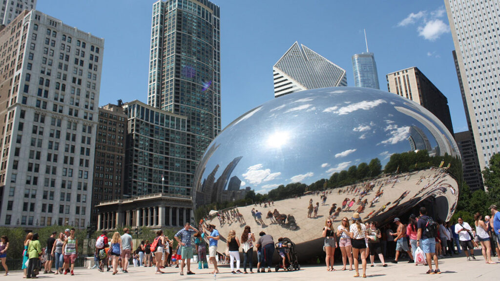 Una imagen del Frjiol (Cloud Gate) en el Parque Milenio en Chicago. Varias personas están en la imagen con atuendos veraniegos.