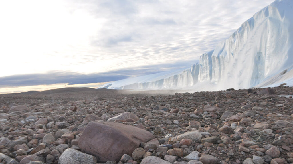 A wall of ice looms over an expanse of rocks.