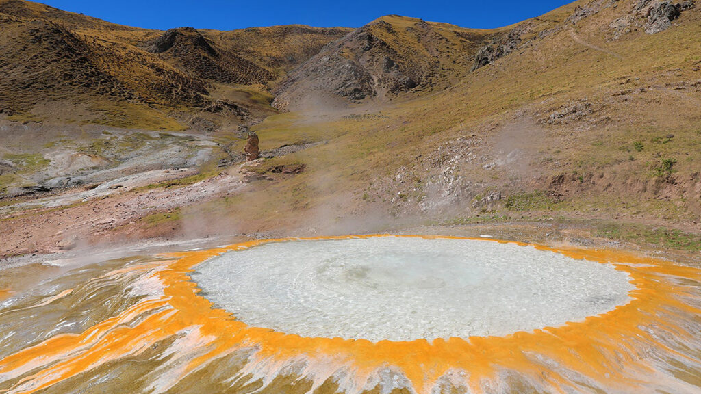 A large hot spring bubbles and steams in the mountains of the Tibetan Plateau.