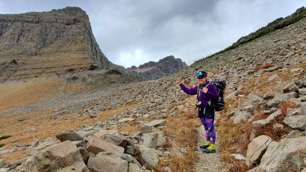 A backpacker points up at a sharp peak above a rocky trail.
