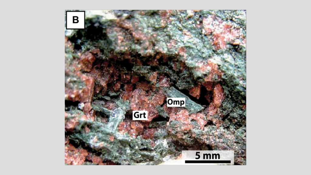 Close-up of an outcrop of an eclogite from the Monviso area of Italy showing a vug, or hole, containing red garnet crystals and green pyroxene crystals.