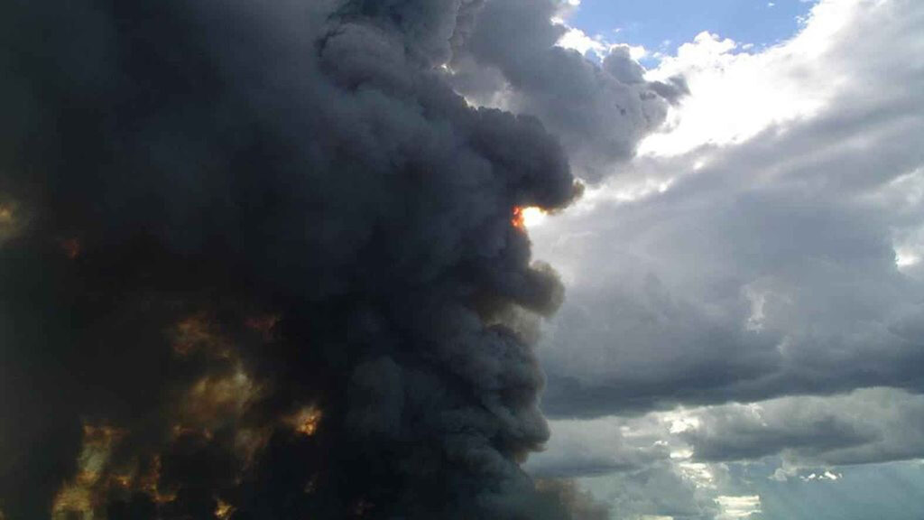 Dark wildfire smoke moves across a partly cloudy sky.