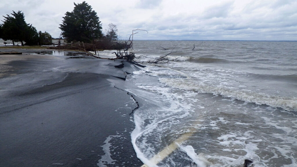 Seawater washes over a cracked roadway along a shoreline