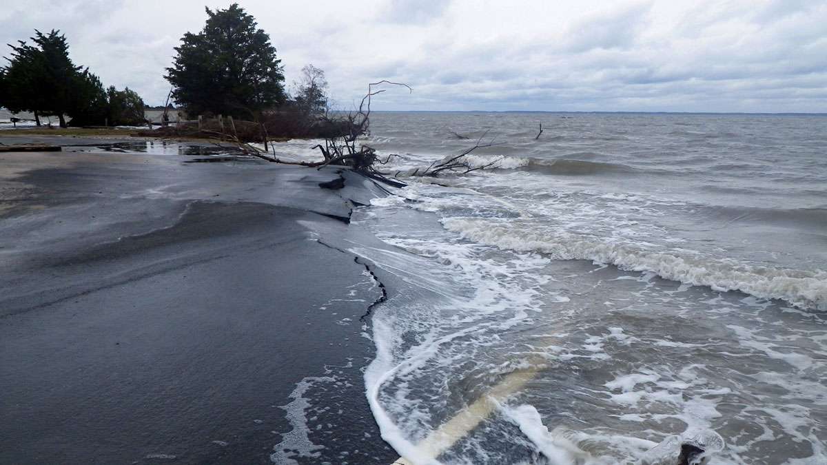 Seawater washes over a cracked roadway along a shoreline