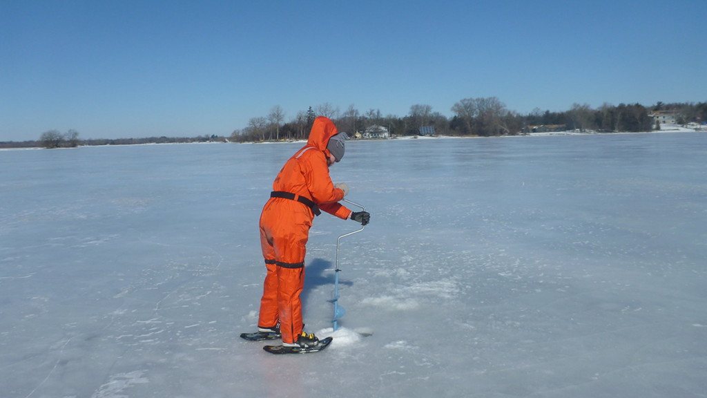 Photo of a scientist drilling into lake ice to take a sample.