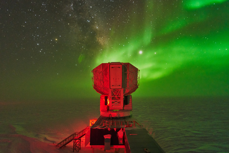 Allen Foster greasing one of the large telescope gears around midwinter underneath the Milky Way and aurorae in 2020. Credit: Geoff Chen