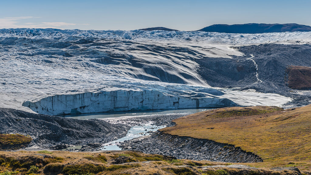A thick, wide expanse of whitish-bluish ice encroaches on what appears to a field of grass.