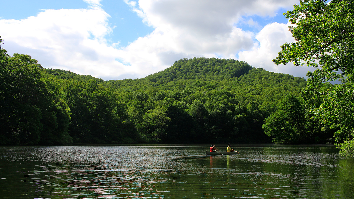 A reservoir surrounded by trees with two people in a canoe