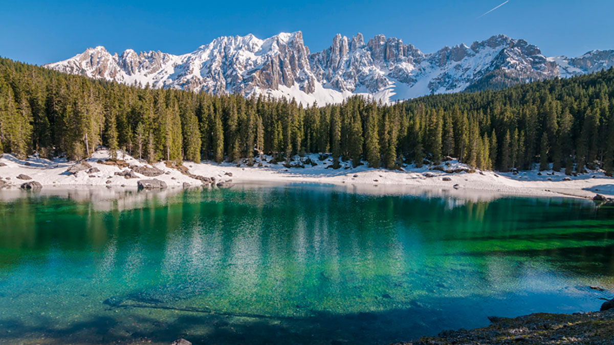 Lake Carezza with evergreens and snowy mountains in the background.