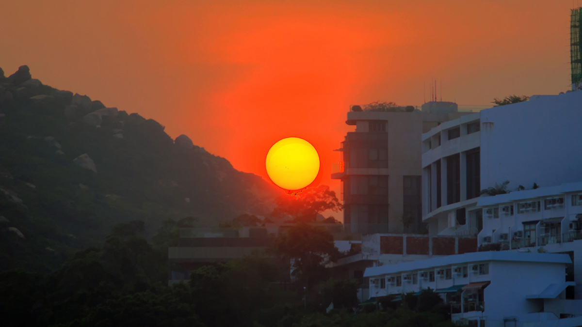 The Sun sets over Hong Kong, with a white building at right.