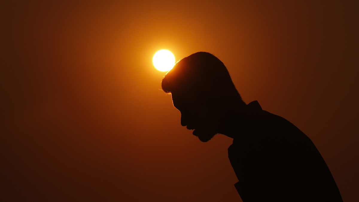Una persona bajando su cabeza con el Sol poniéndose en el fondo.