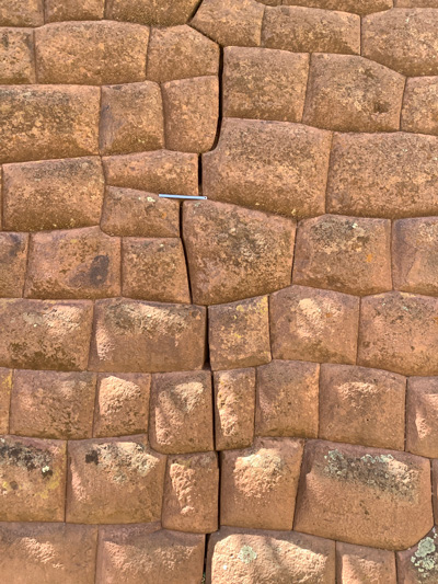 Fotografía de una pared de un edificio inca marrón con una fractura vertical cortando todo el muro. Se muestra un pequeño lápiz como escala para la foto.