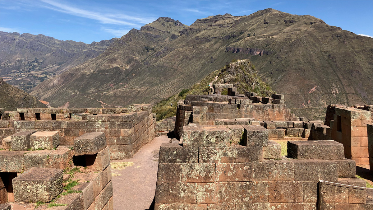 Edificios inca marrones con una calle en medio. Al fondo se distinguen los Andes y un cielo azul con pocas nubes.