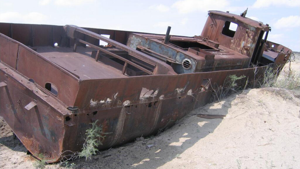 A rusty fishing boat sits in a sandy desert.