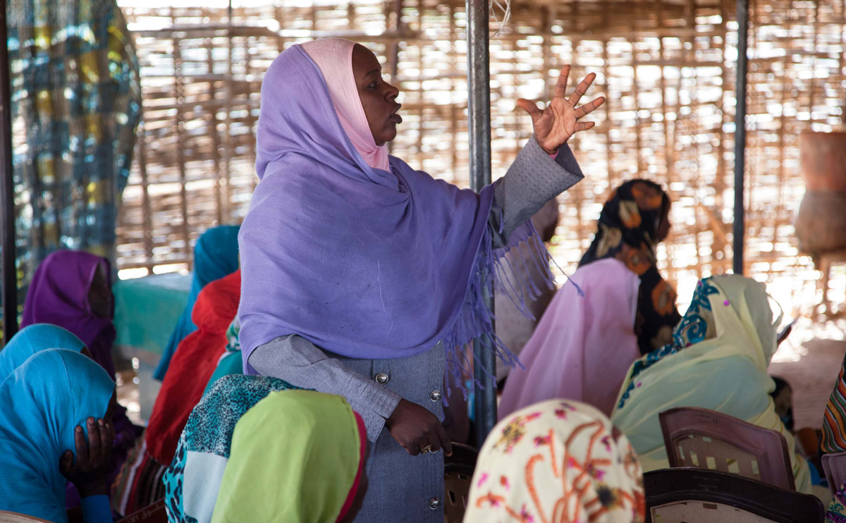 A woman wearing a light purple hijab stands in a meeting to talk.