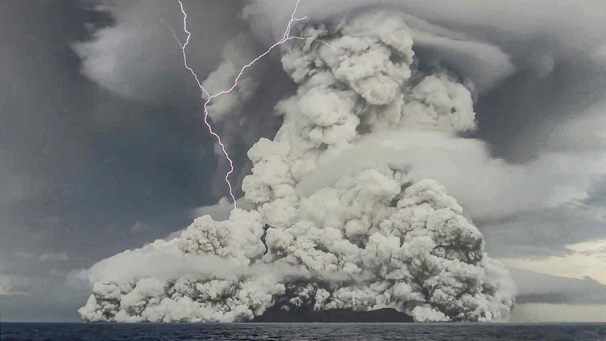Un rayo aparece en medio de nubes de cenizas y vapor que están saliendo de volcán a la atmósfera sobre el océano.