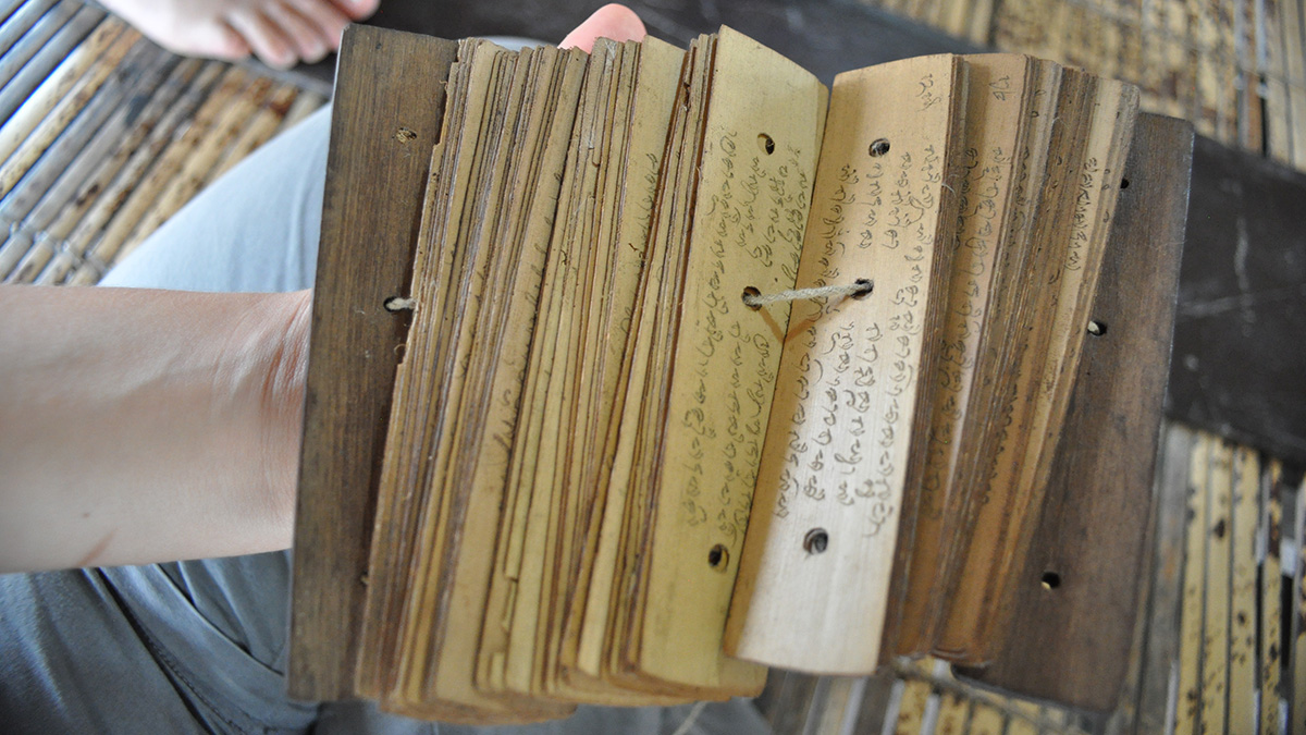Close-up of the palm leaves of Babad Lombok held together by a string threaded through a hole in each page. Each side of the palm leaves shows inscriptions in Old Javanese.