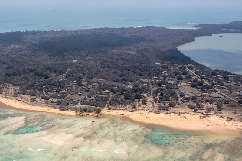 Aerial photo of an island in the nation of Tonga, showing buildings covered in ash and bare trees