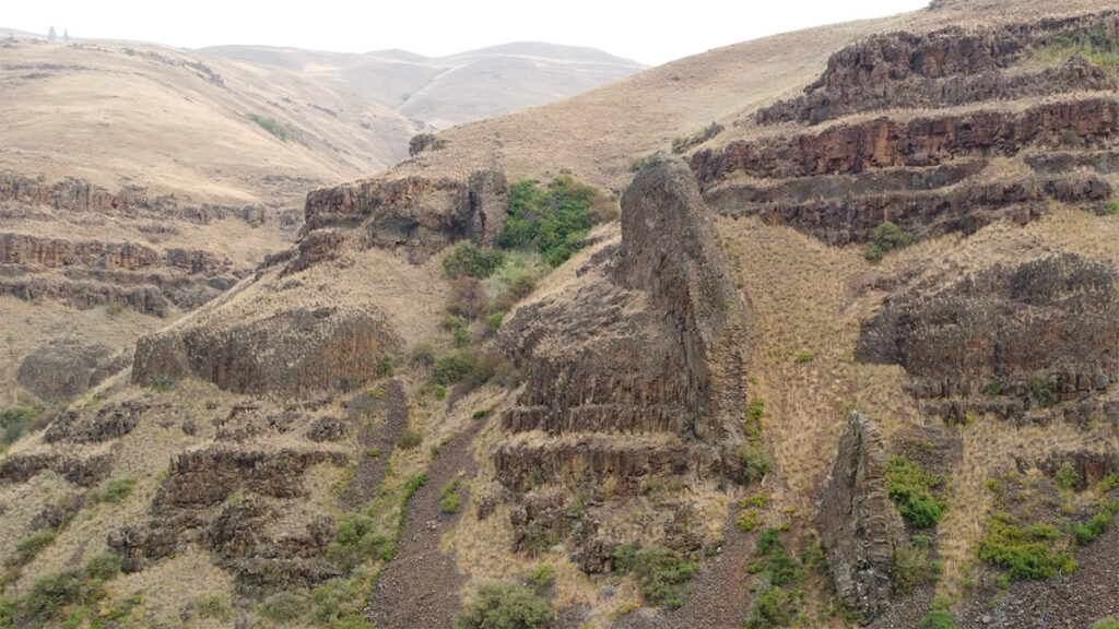 View of steep hills with exposures of dark rock as well as patches of green vegetation