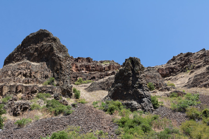 Dark vertical rock outcrops protrude from the surrounding rock on a rugged hillside with patches of vegetation.
