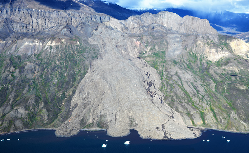 Aerial image of the 2021 landslide, showing the debris path spilling into the ocean. Whereas the landslide path is brown and gray, the surrounding slope is still green with vegetation.