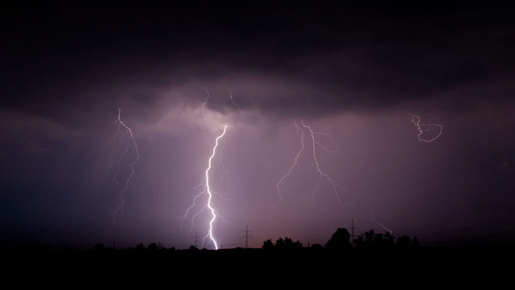 Four bolts of lightning strike the ground simultaneously against a purple sky.