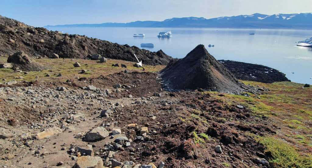 Image from the coast at the base of the 2021 landslide shows Kristian Svennevig sitting next to a cone-shaped pile of rocky debris called a molard