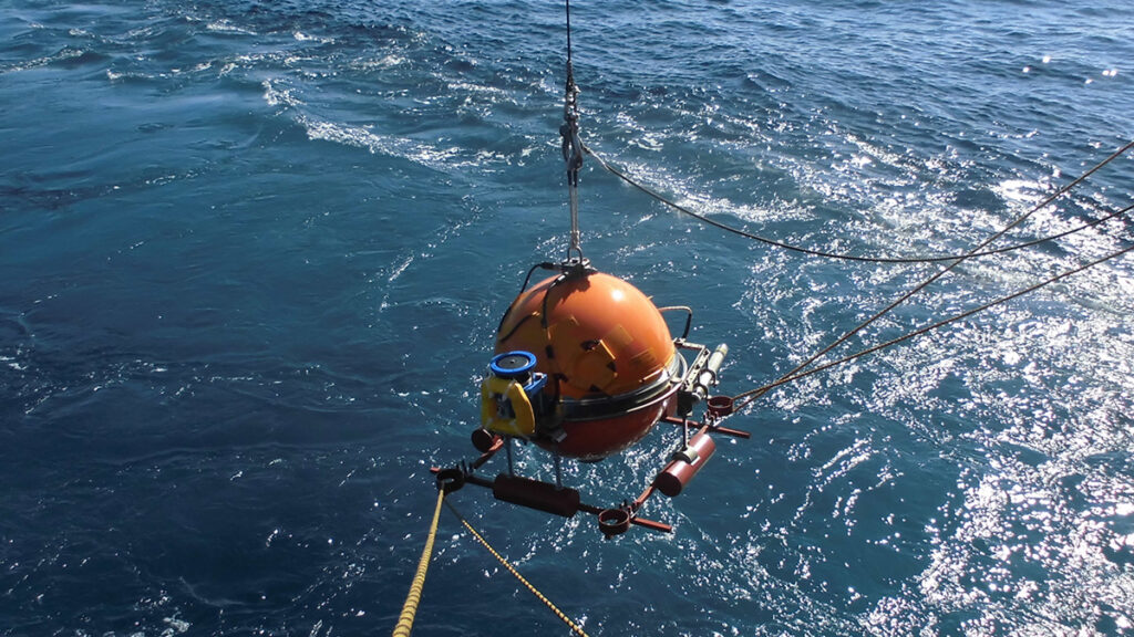 An orb-shaped ocean bottom seismometer descending into the sea surface