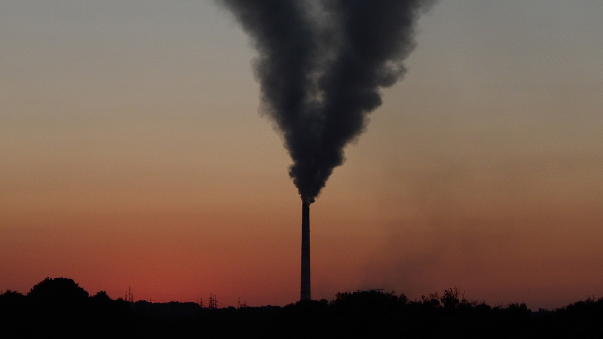 The silhouette of a power plant emitting a billowing smoke cloud against a sunset background