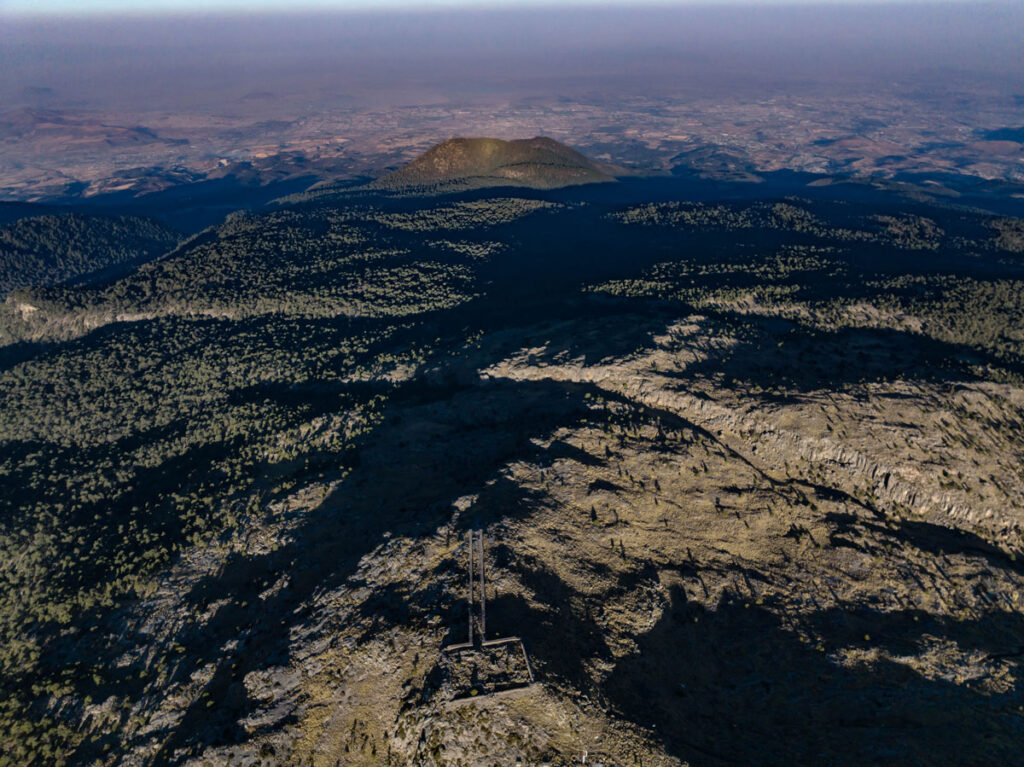 Photo of hills with trees and long shadows. Rectangular structure in foreground.