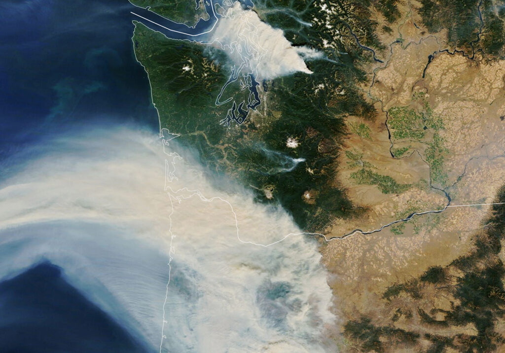 Satellite image of tan whisps of clouds over green land. There is brown land to the right and blue ocean to the left.