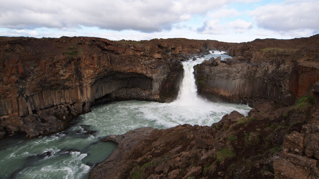 Photo of a brown landscape with a waterfall in the center flowing into a turbulent pool